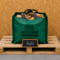 Green bag of firewood labeled 'North Shore Firewood' on a wooden pallet with a sign indicating 'Ash'.