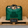 Green bag with firewood labeled 'North Shore Firewood' on a wooden pallet with a 'Birch' sign.