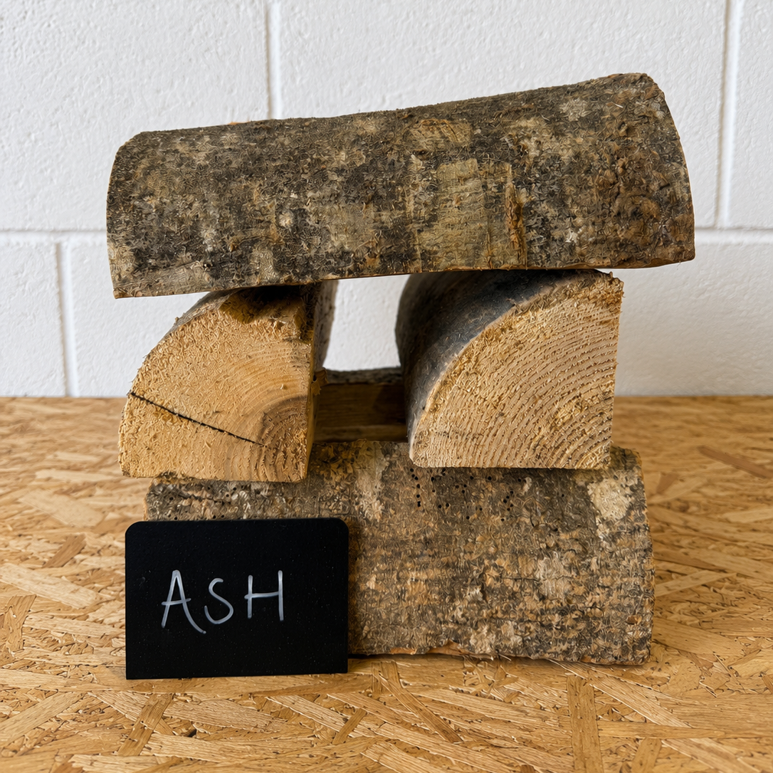Stack of firewood with a small blackboard labeled 'ASH' on a wooden surface.