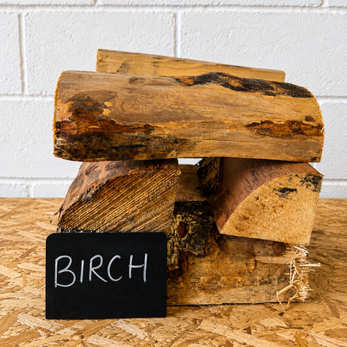 Stack of birch logs on a wooden surface with a white tiled wall background