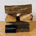 Stack of hornbeam firewood with a small black sign on a wooden surface.