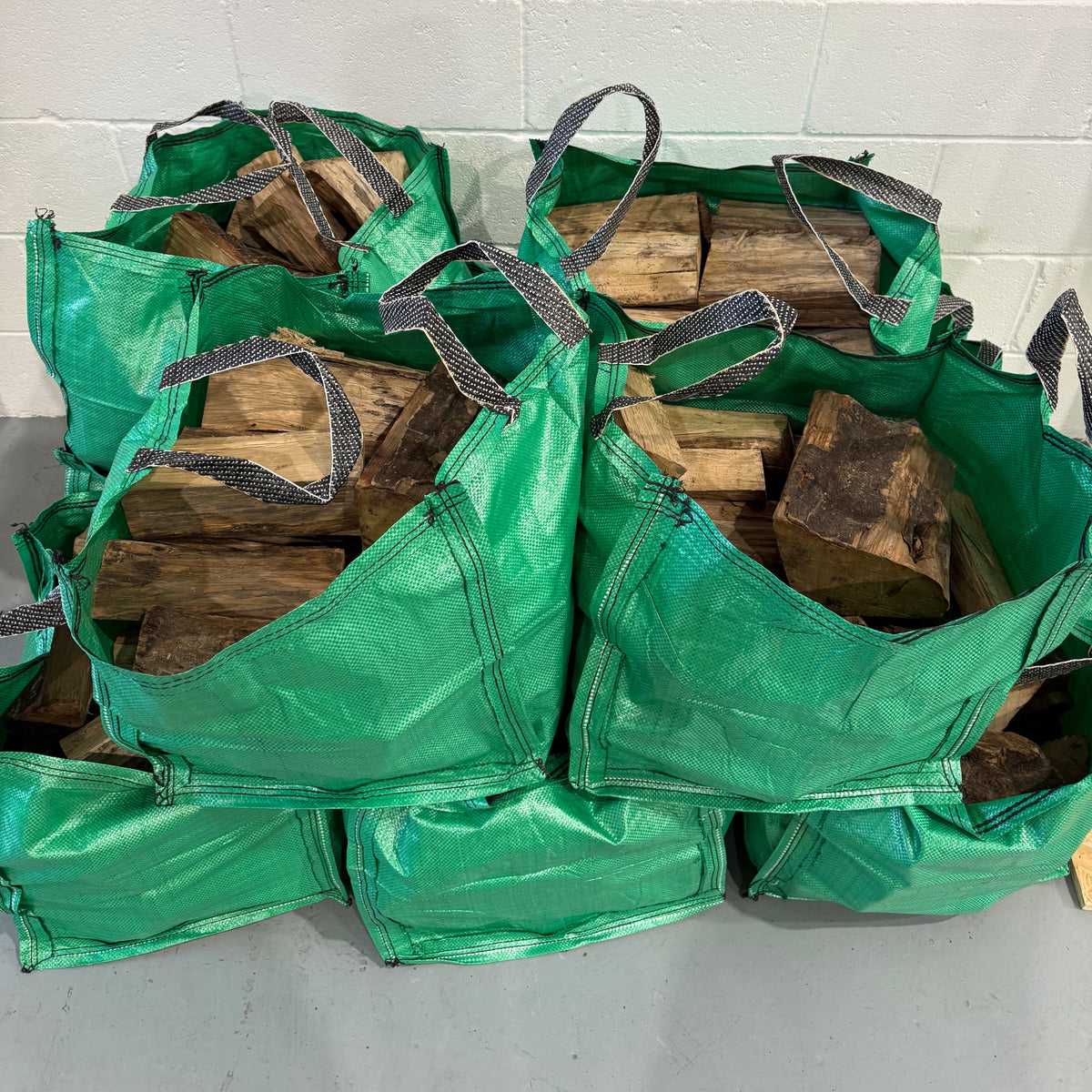 Green Hornbeam firewood storage bag filled with wood against a white wall.