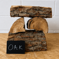 Stack of wooden logs with a small blackboard labeled 'Oak' on a wooden surface.