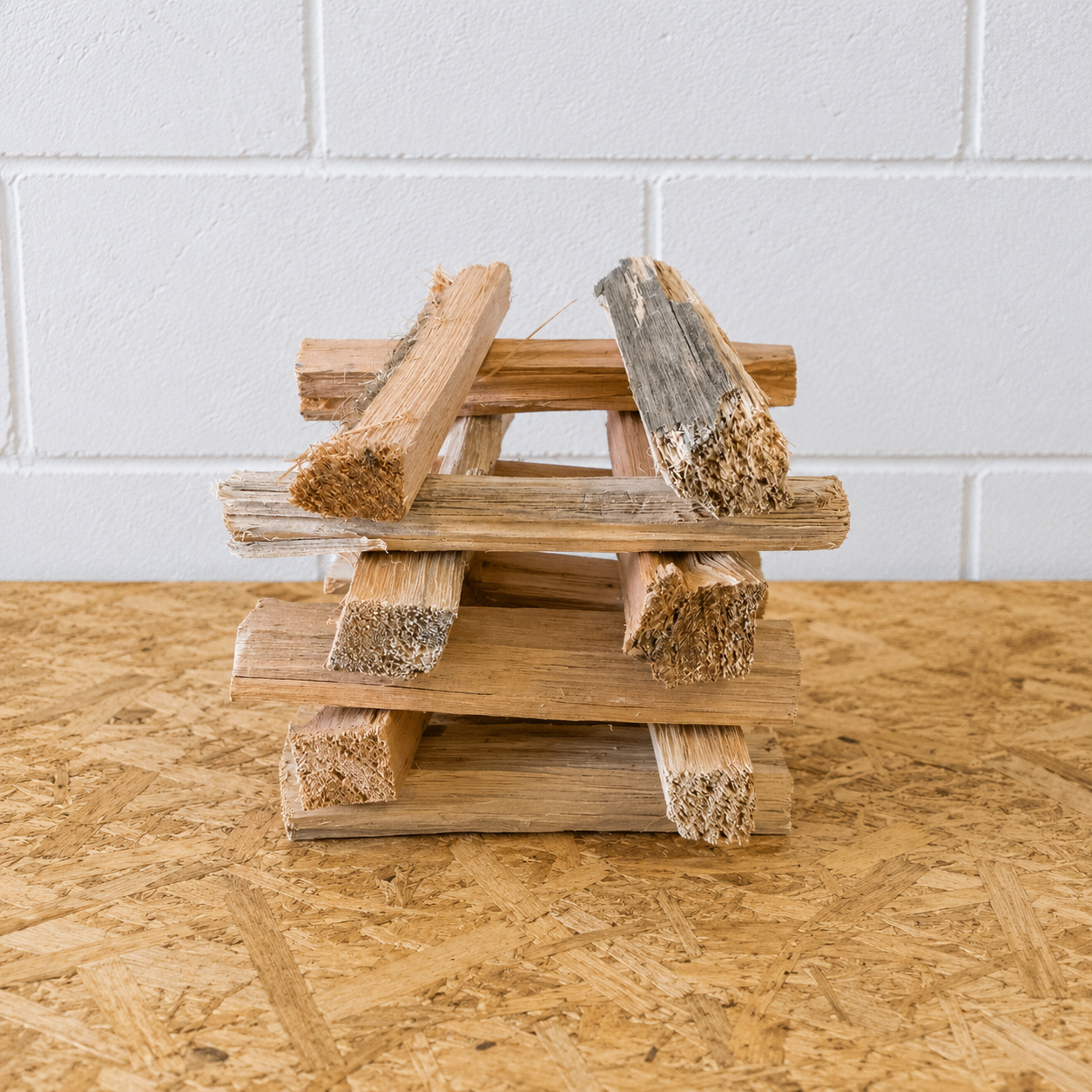 Stack of wooden logs on a wooden surface with a white tiled wall background